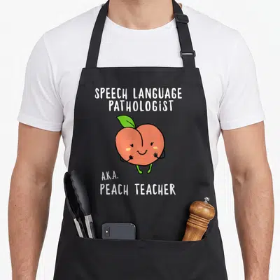 Speech teacher apron - Cartoon orange peach with green leaf and white text reading Speech Language Pathologist AKA — shown on a black cotton canvas apron against a white background