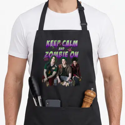 Channel zombie apron - Three green-haired zombies sit below dripping text reading KEEP CALM AND ZOMBIE — shown on a black cotton canvas apron against a white background