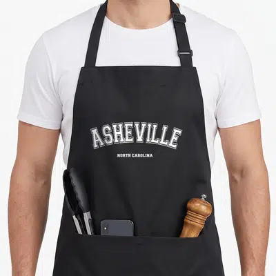 Cute north asheville apron - White ASHEVILLE NORTH CAROLINA text stacked on grey background — shown on a black cotton canvas apron against a white background