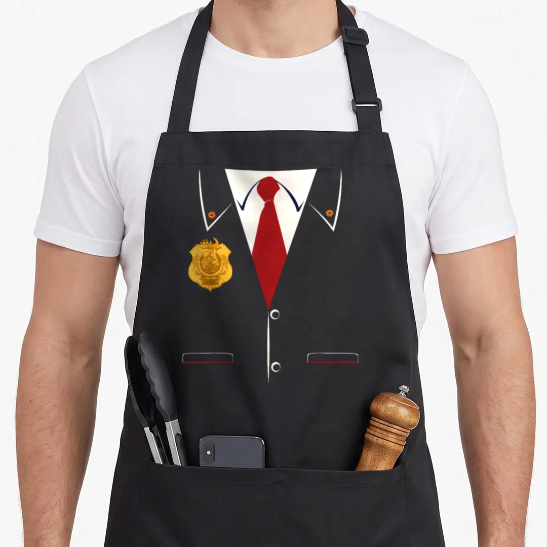 Odd son squad apron - Grey uniform chest with red tie, gold badge, and white collar buttons — shown on a black cotton canvas apron against a white background