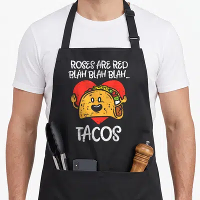Rose valentine's day apron - Cartoon taco with face over red heart and text Roses Are Red Blah Blah Blah Tacos — shown on a black cotton canvas apron against a white background