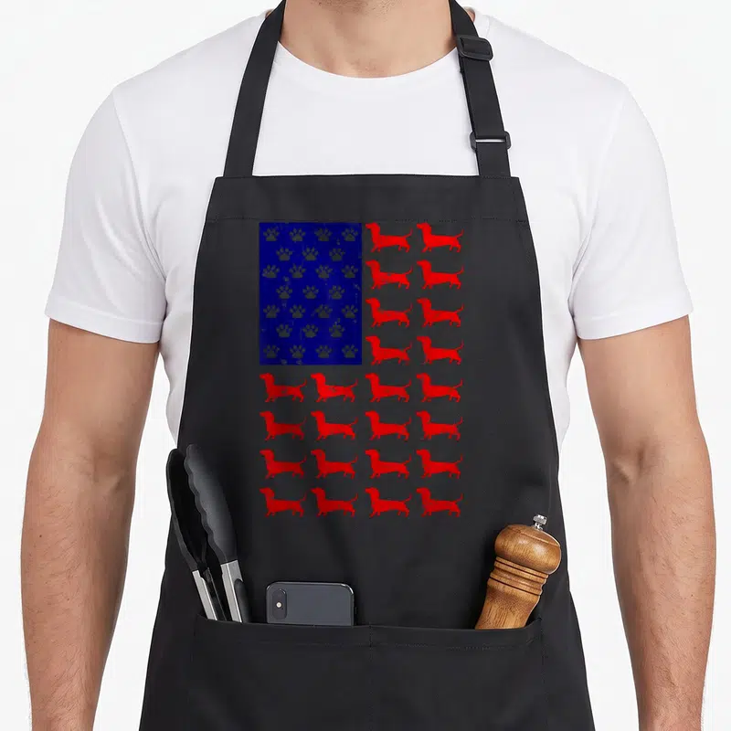 4th dachshund apron - Red dachshund rows and blue rectangle with white paw prints in distressed flag style — shown on a black cotton canvas apron against a white background