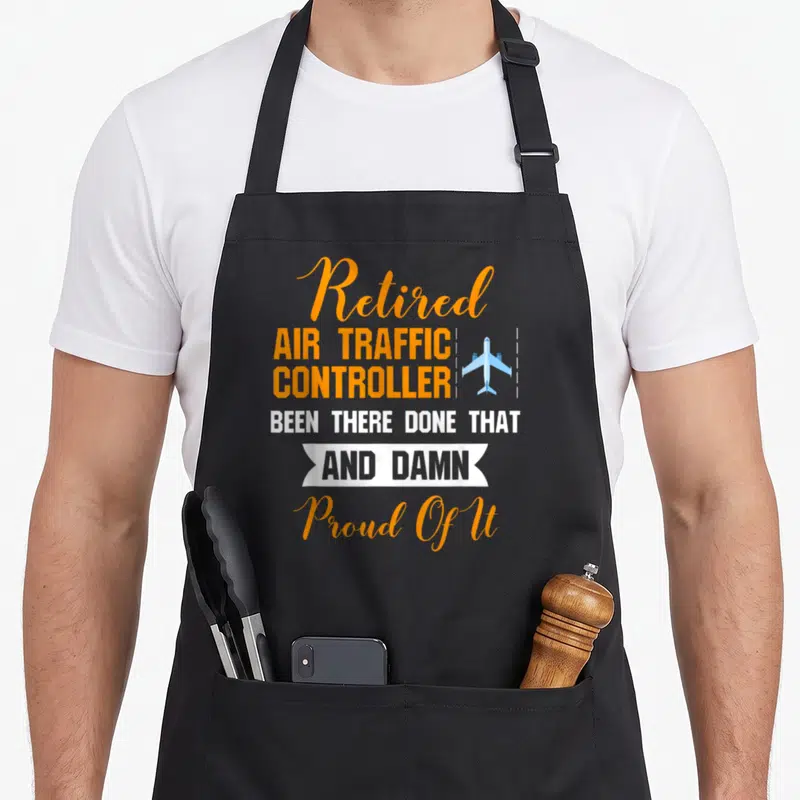 Proud air traffic controller apron - Stacked orange and white text reading Retired Air Traffic Controller with blue — shown on a black cotton canvas apron against a white background