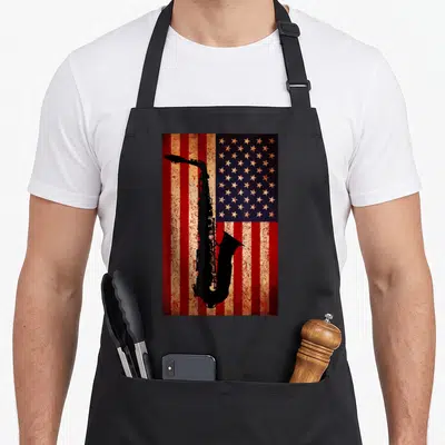 Saxophone american flag apron - Black saxophone silhouette on distressed red white and blue American flag — shown on a black cotton canvas apron against a white background
