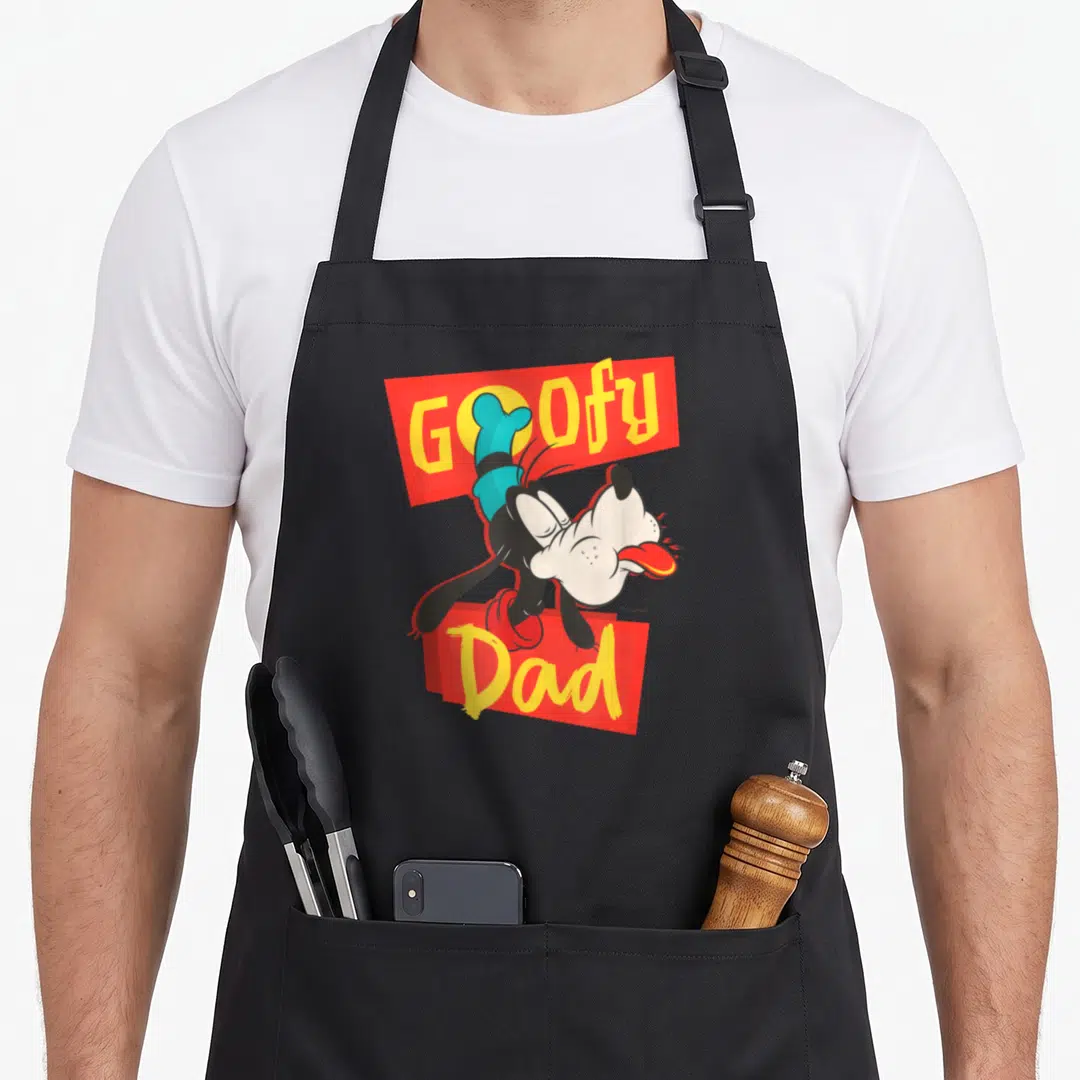 Family trip father day apron - Goofy Dad cartoon print with red banners and yellow lettering — shown on a black cotton canvas apron against a white background