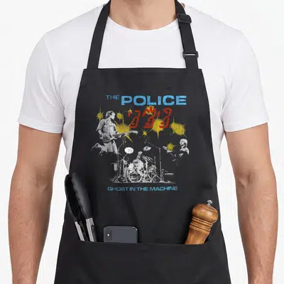Rock police apron - Distressed white band silhouettes with blue text and yellow red splatters — shown on a black cotton canvas apron against a white background