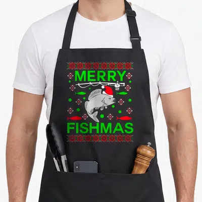 Fishmas merry christmas apron - Cartoon fish in Santa hat under fishing rod with green and red dots and MERRY FISHMAS — shown on a black cotton canvas apron against a white background