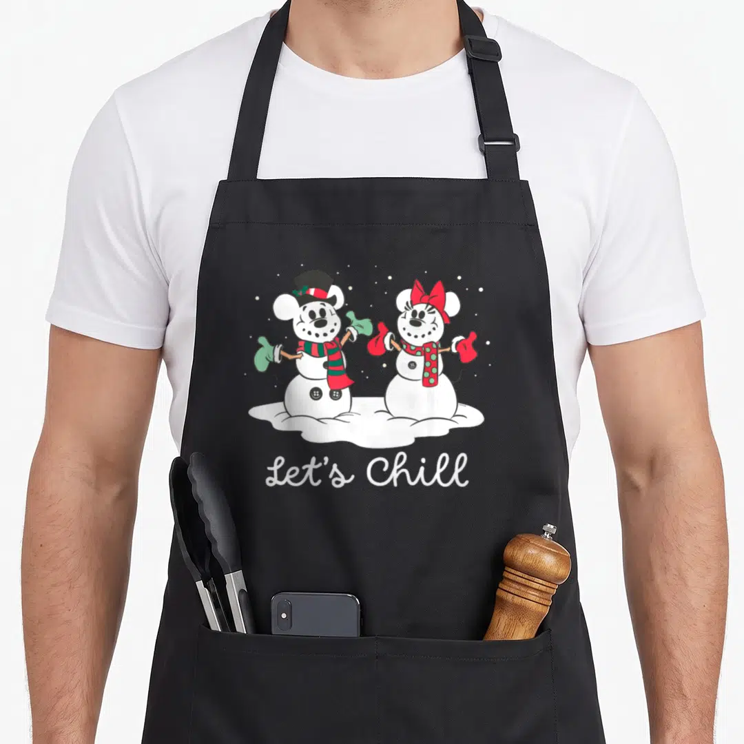 Snowmen holiday apron - Two cartoon snowmen in red and green scarves with Let's Chill text below — shown on a black cotton canvas apron against a white background