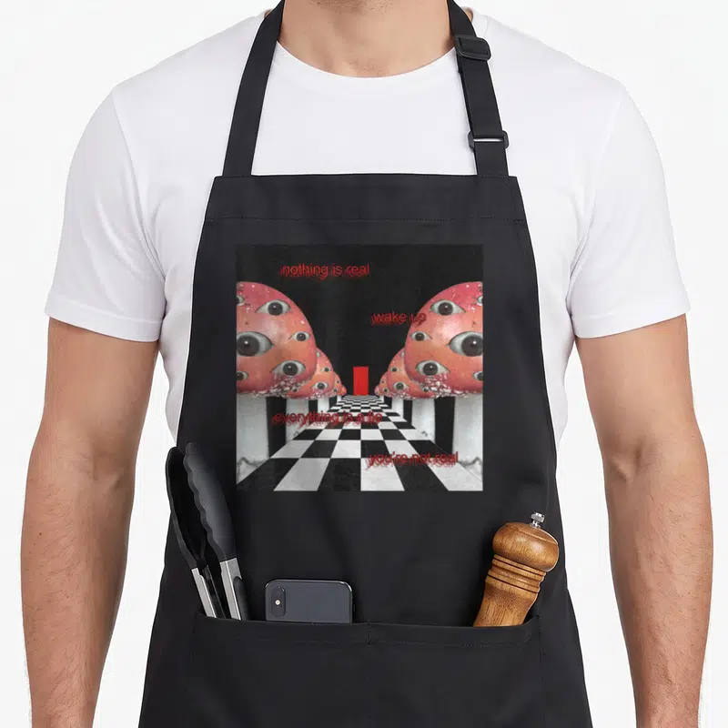 Weirdcore mushroom apron - Red mushrooms with eyes on checkerboard floor with glitchy red text — shown on a black cotton canvas apron against a white background