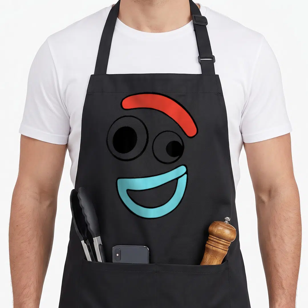 Face camping apron - Minimalist face with red eyebrow, two mismatched black eyes, light blue smiling mouth — shown on a black cotton canvas apron against a white background