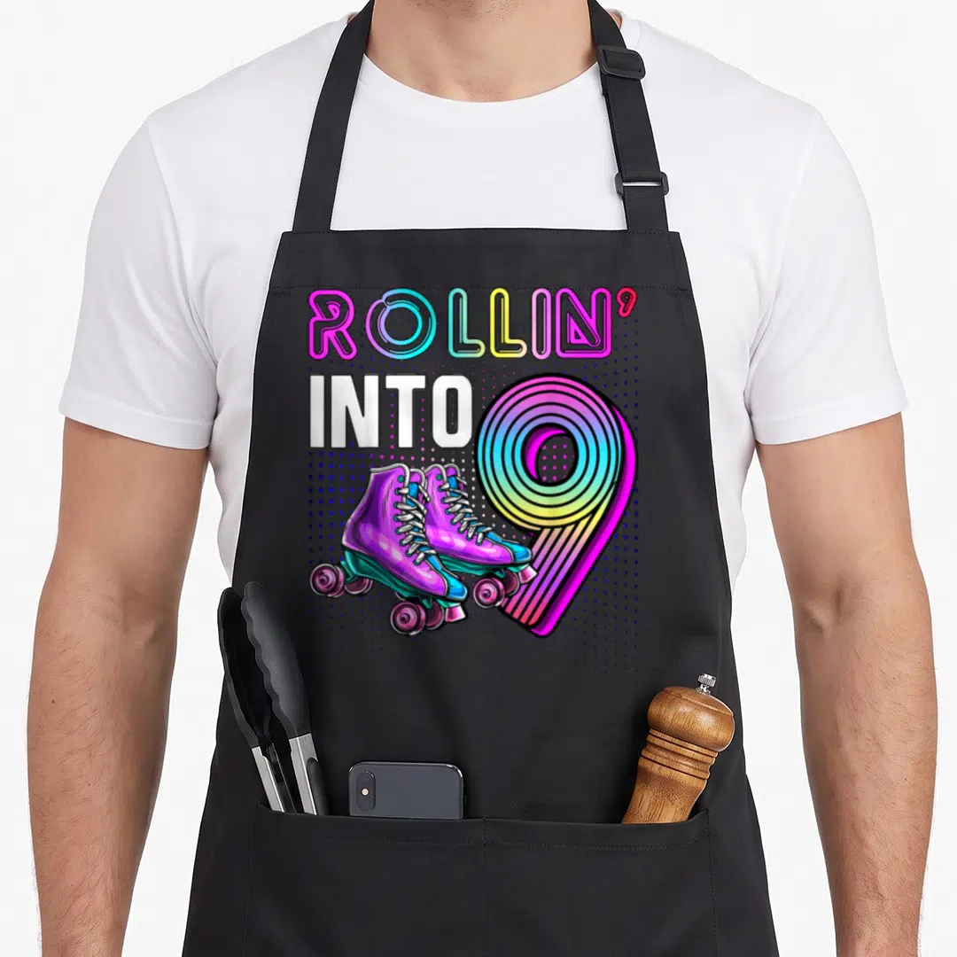 Rink birthday apron - Rollin' Into 9 text with purple roller skates and rainbow number nine — shown on a black cotton canvas apron against a white background