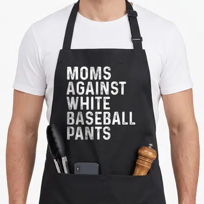 Against baseball apron - White distressed text stacked reading MOMS AGAINST WHITE BASEBALL PANTS — shown on a black cotton canvas apron against a white background