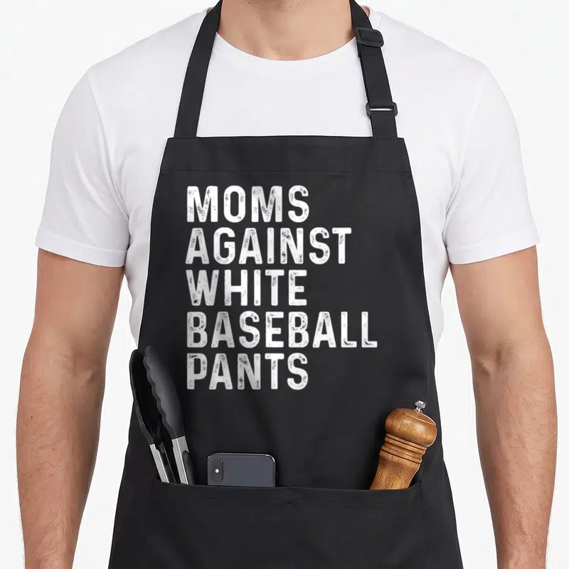 Against baseball apron - White distressed text stacked reading MOMS AGAINST WHITE BASEBALL PANTS — shown on a black cotton canvas apron against a white background