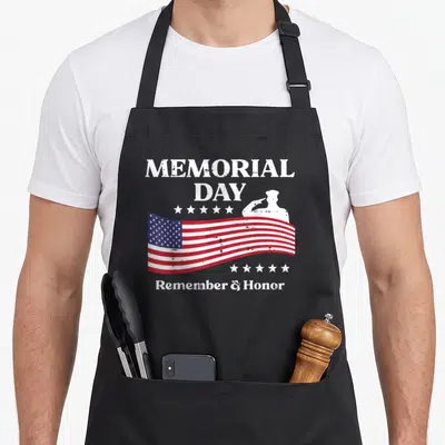 Memorial patriots apron - Distressed USA flag with saluting soldier silhouette and MEMORIAL DAY text surrounded by stars — shown on a black cotton canvas apron against a white background