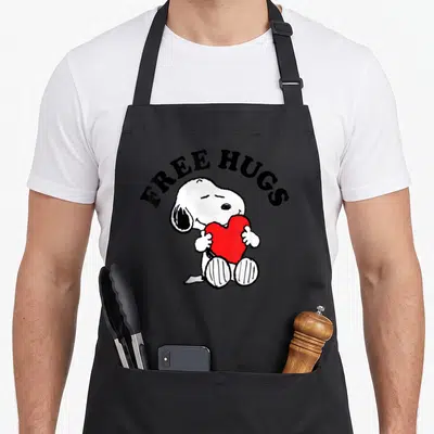 Free little miss apron - Snoopy sitting and hugging a large red heart under arched black text reading FREE HUGS — shown on a black cotton canvas apron against a white background