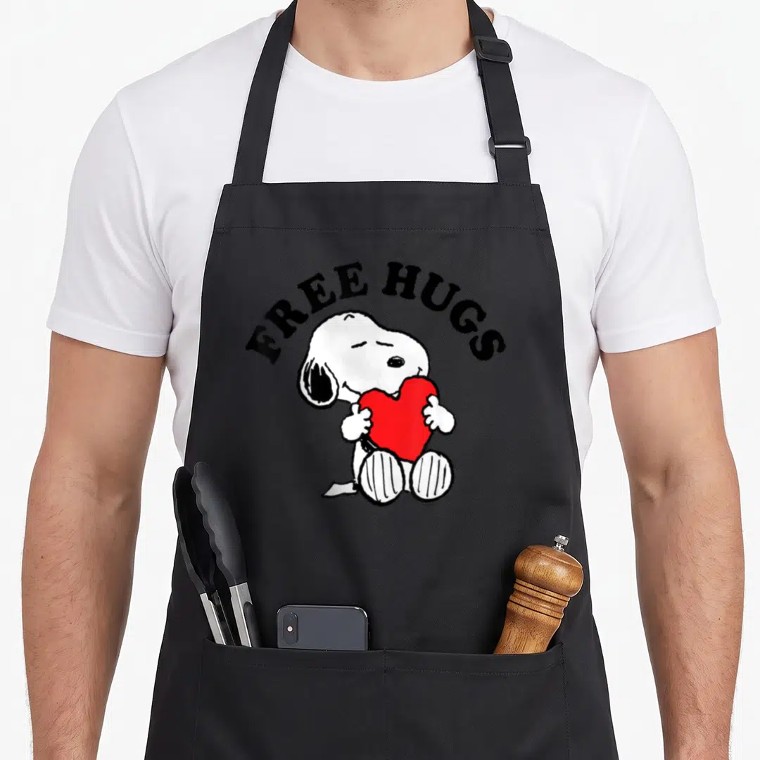 Free little miss apron - Snoopy sitting and hugging a large red heart under arched black text reading FREE HUGS — shown on a black cotton canvas apron against a white background