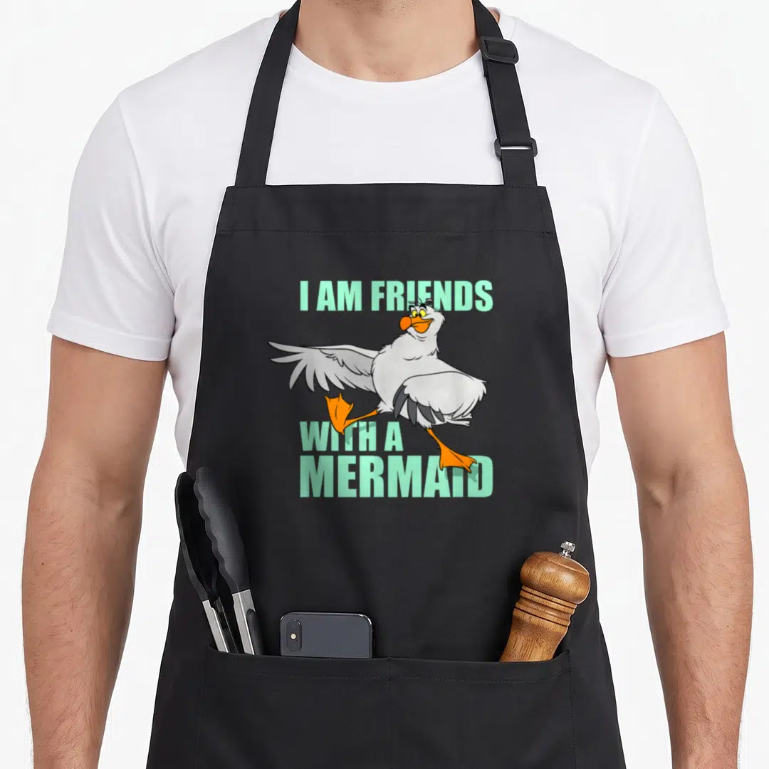 Scuttle friends apron - Cartoon seagull with orange feet and mint text I AM FRIENDS WITH A MERMAID — shown on a black cotton canvas apron against a white background