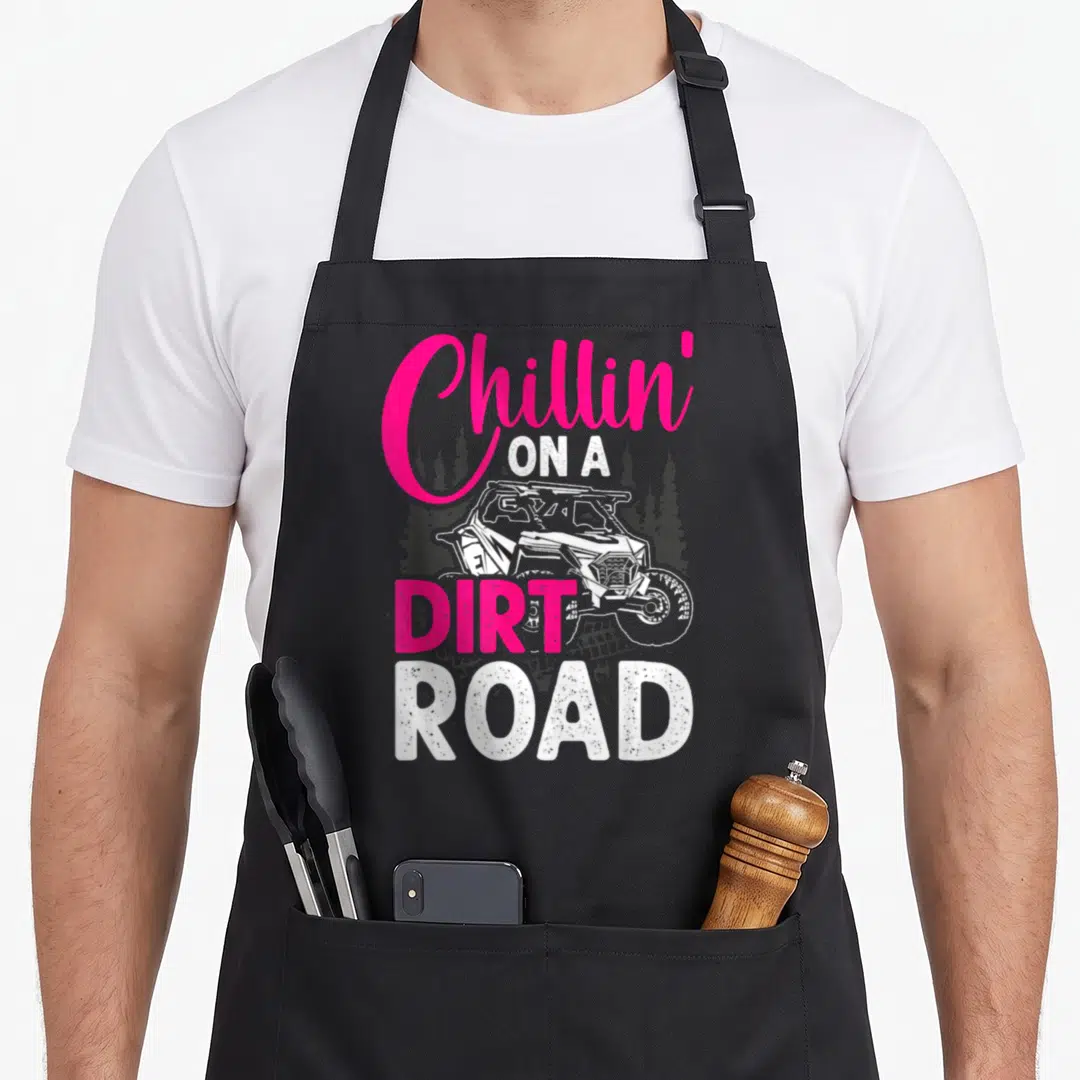 Chillin road apron - Pink and white Chillin On A Dirt Road text with UTV and pine trees — shown on a black cotton canvas apron against a white background