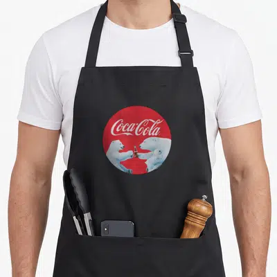 Coca bear apron - Polar bears holding bottle inside red circle with white Coca-Cola script — shown on a black cotton canvas apron against a white background