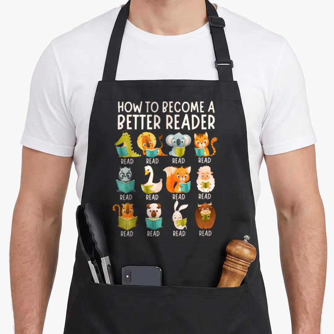 Become teacher apron - 12 cartoon animals holding books with READ text under each in 3x4 grid — shown on a black cotton canvas apron against a white background