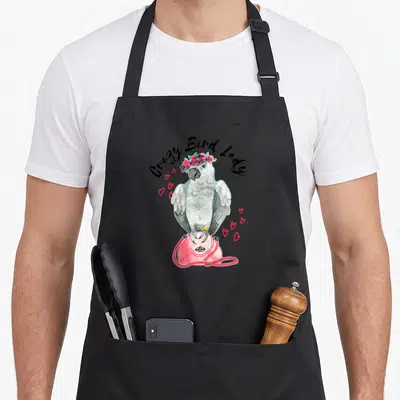 Parrot watercolor bird apron - Grey parrot with flower crown on pink bag under Crazy Bird Lady text — shown on a black cotton canvas apron against a white background