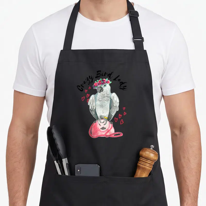 Parrot watercolor bird apron - Grey parrot with flower crown on pink bag under Crazy Bird Lady text — shown on a black cotton canvas apron against a white background