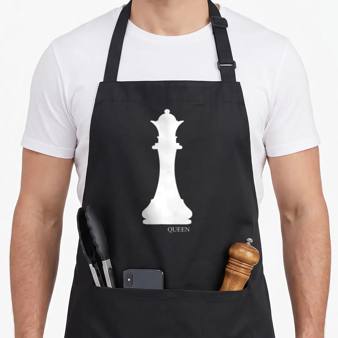 Chess halloween apron - White chess queen silhouette above the word QUEEN in minimalist style — shown on a black cotton canvas apron against a white background
