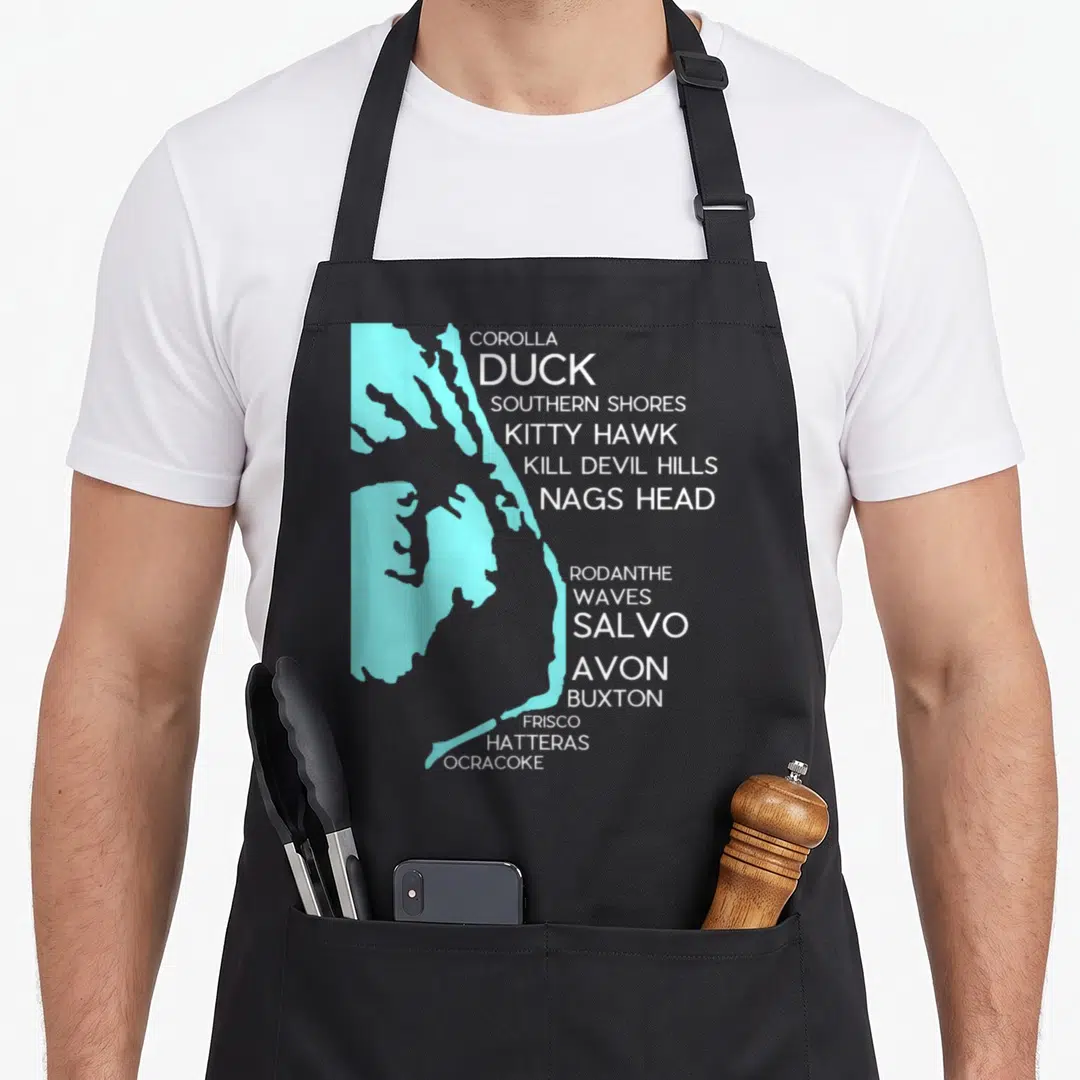 Outer duck lady apron - Light blue Outer Banks map with white town names like Duck and Salvo on a dark background — shown on a black cotton canvas apron against a white background