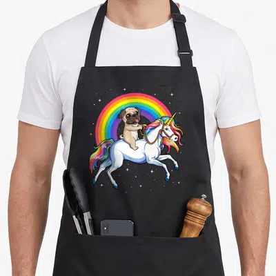Pug rainbow apron - Cartoon pug riding leaping unicorn under rainbow with white stars — shown on a black cotton canvas apron against a white background