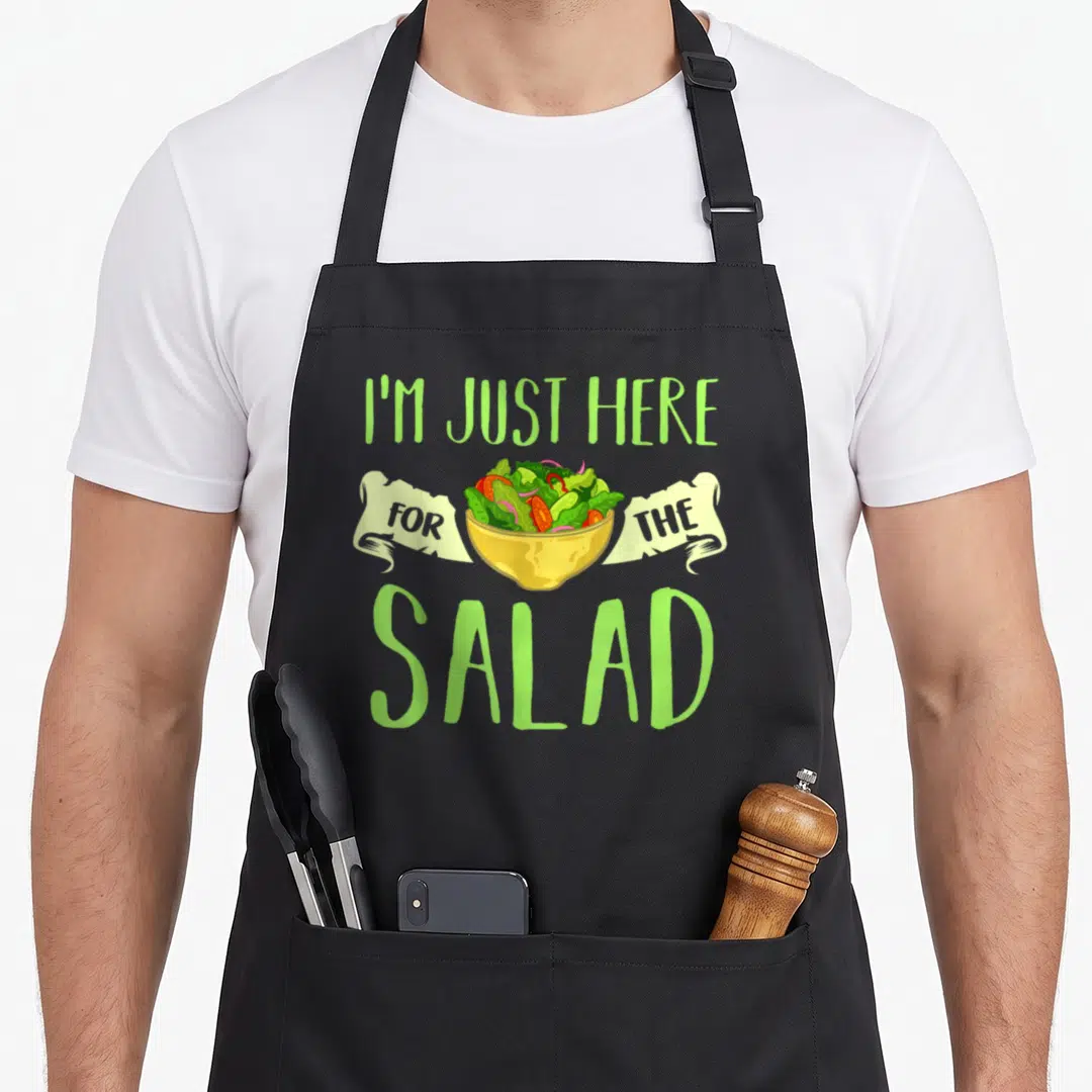 Salad vegan apron - Cartoon salad bowl with I'm Just Here For The Salad text in lime green — shown on a black cotton canvas apron against a white background