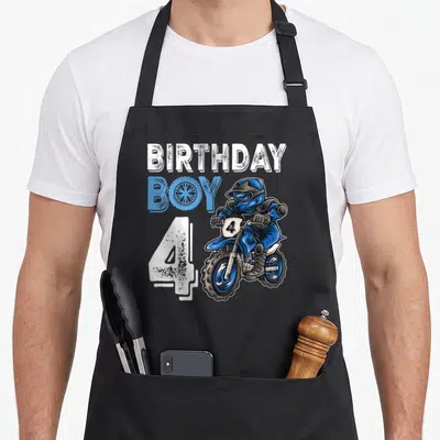 Motocross birthday apron - Cartoon motocross rider with BIRTHDAY BOY 4 text in blue and white — shown on a black cotton canvas apron against a white background