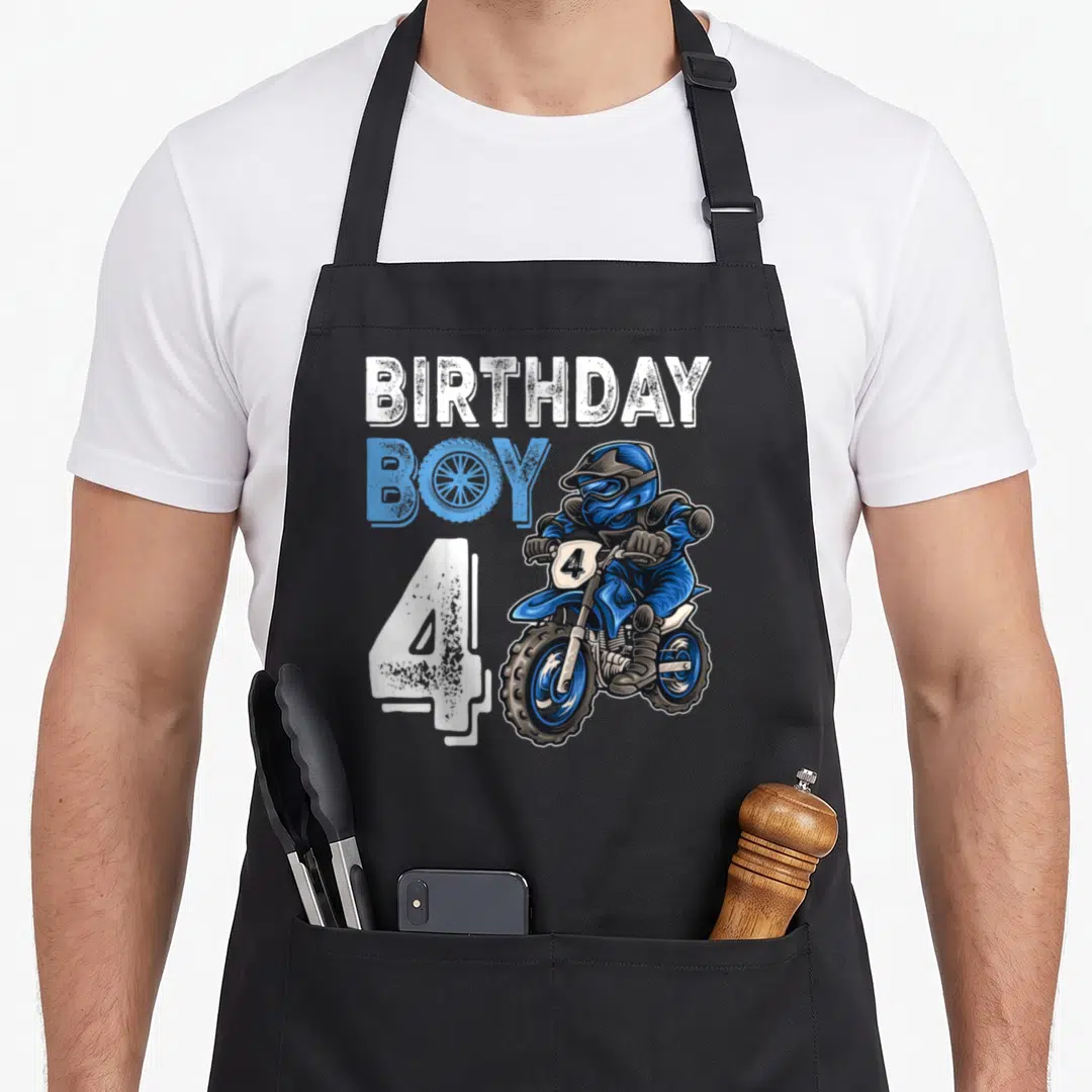 Motocross birthday apron - Cartoon motocross rider with BIRTHDAY BOY 4 text in blue and white — shown on a black cotton canvas apron against a white background