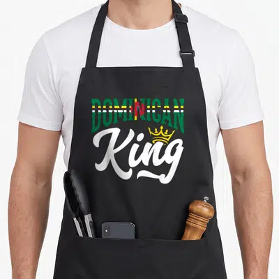 Dominica king apron - DOMINICAN flag text and yellow crown on King script — shown on a black cotton canvas apron against a white background