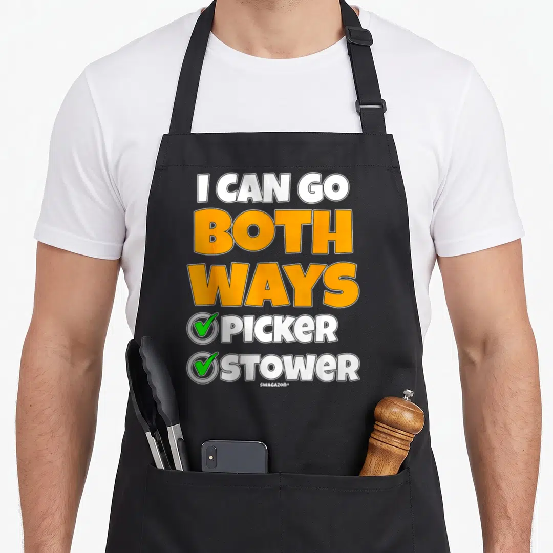 Both pickers apron - Stacked text I CAN GO BOTH WAYS PICKER STOWER with green checkmarks in grey circles on black fabric — shown on a black cotton canvas apron against a white background