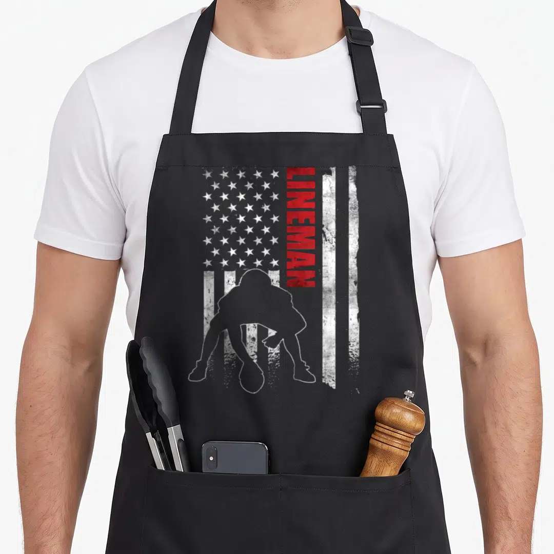 Offensive american flag apron - White football player silhouette over distressed flag with vertical red LINEMAN text — shown on a black cotton canvas apron against a white background