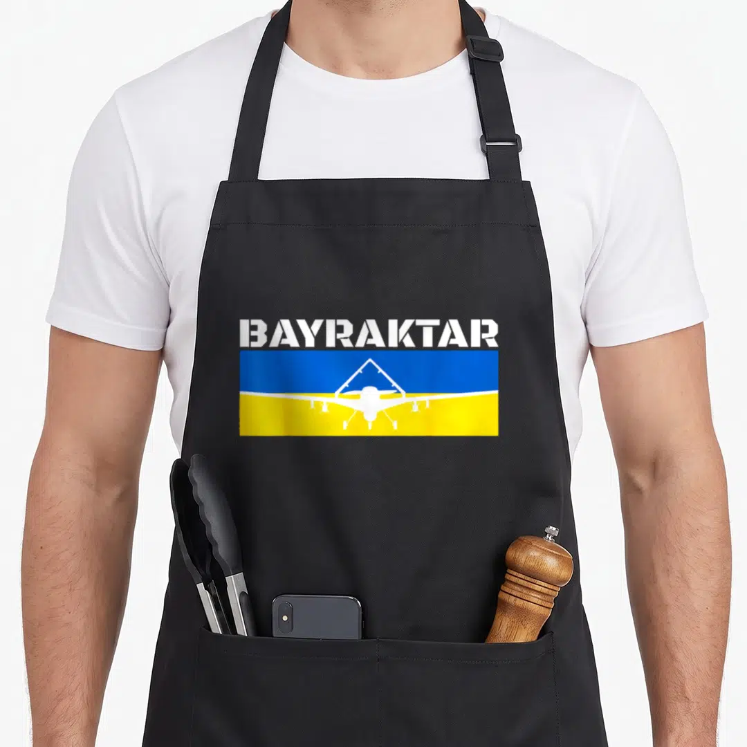 Bayraktar turkish apron - White drone silhouette on blue and yellow flag with BAYRAKTAR text — shown on a black cotton canvas apron against a white background