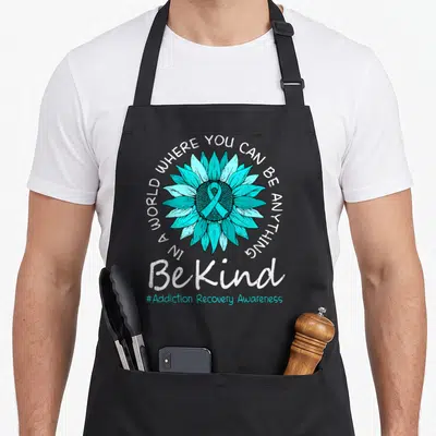 Kind ribbon apron - Teal sunflower with awareness ribbon and Be Kind text on black apron — shown on a black cotton canvas apron against a white background