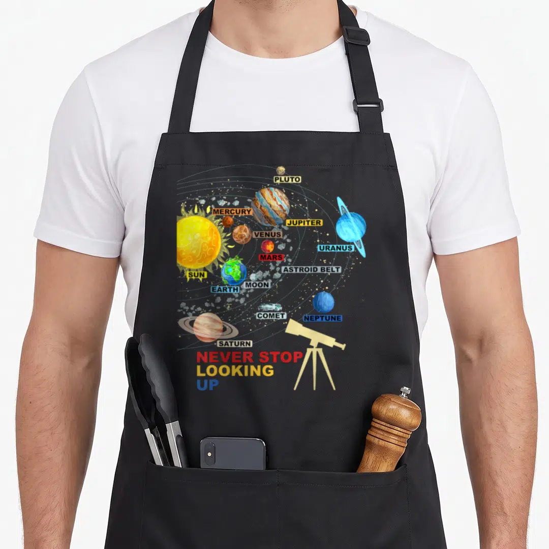 Stop space planets apron - Cartoon solar system diagram with labeled planets, asteroid belt, comet, and telescope next — shown on a black cotton canvas apron against a white background