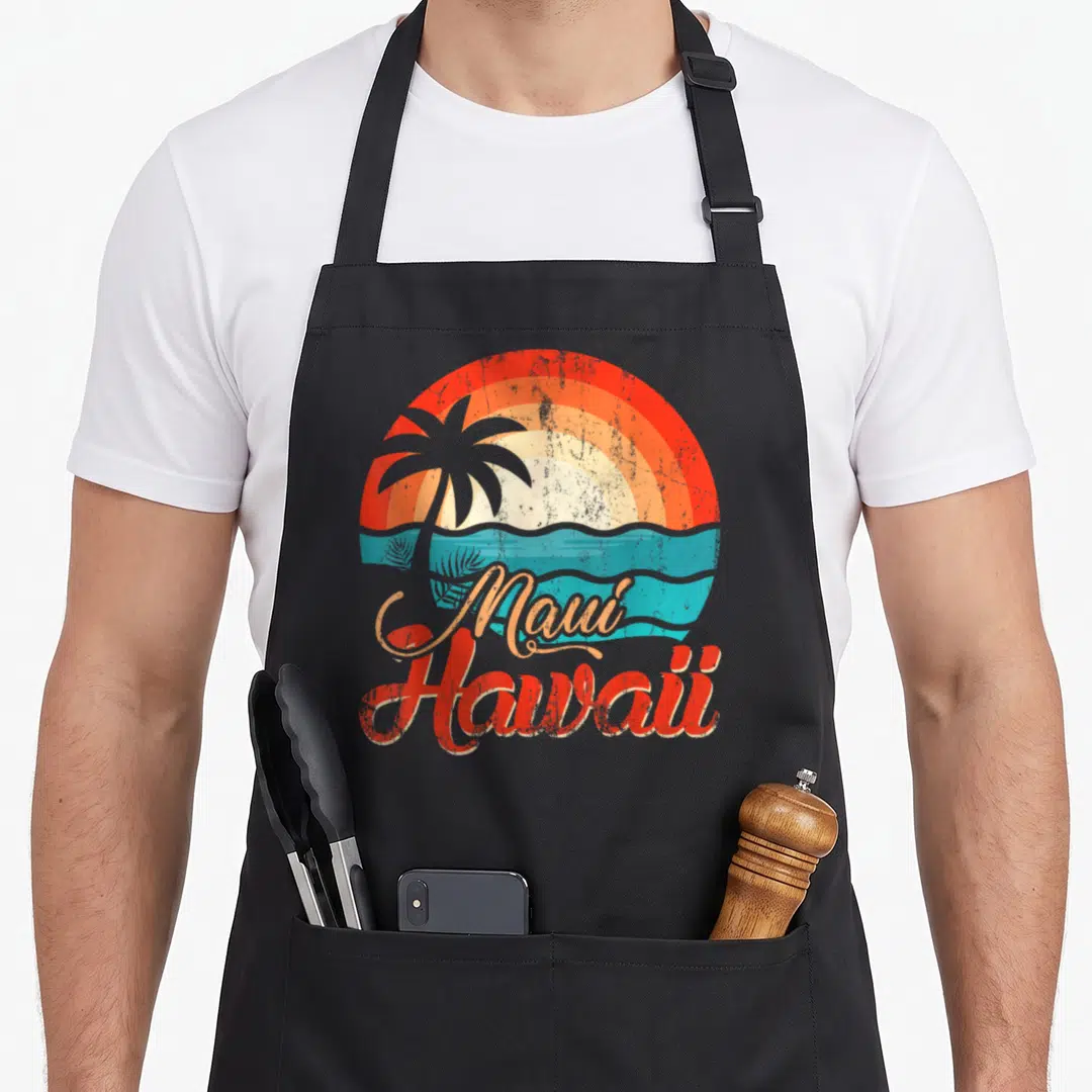 Honolulu tree apron - Retro sunset with palm tree silhouette, teal waves, and 'Maui Hawaii' script text in red — shown on a black cotton canvas apron against a white background