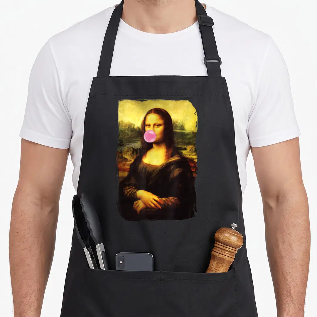 Blowing mona lisa apron - Mona Lisa portrait with pink bubblegum bubble over mouth in yellow brown photo style — shown on a black cotton canvas apron against a white background