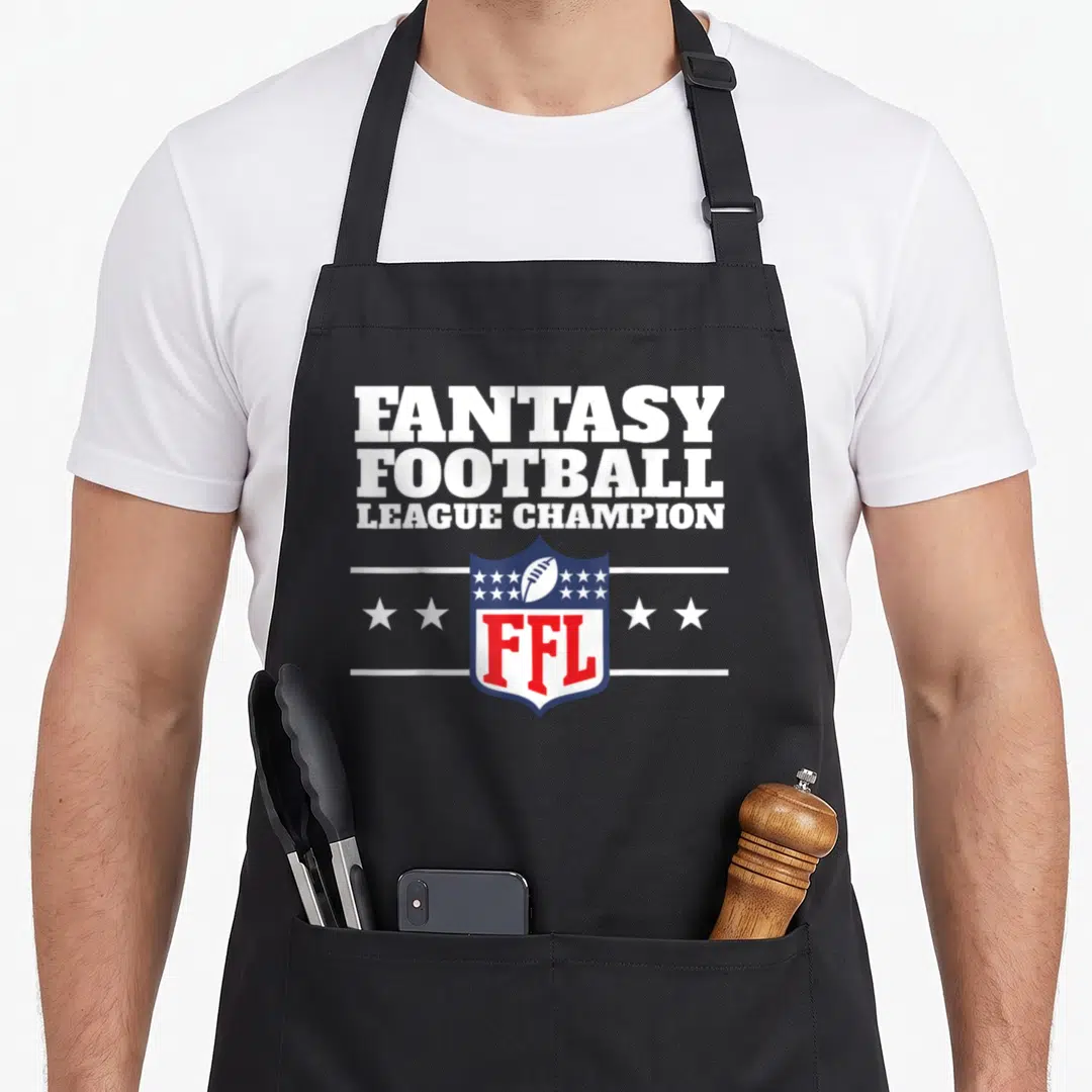 League football apron - White text FANTASY FOOTBALL LEAGUE CHAMPION above blue red shield with football and stars — shown on a black cotton canvas apron against a white background