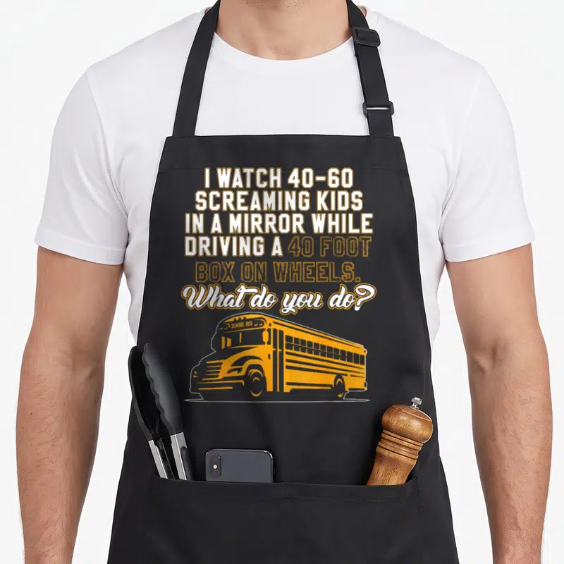 School bus driver omnibus apron - Yellow school bus graphic below stacked white and yellow text about watching — shown on a black cotton canvas apron against a white background