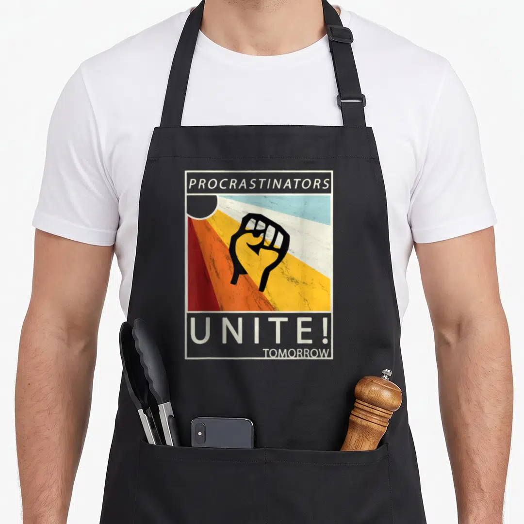 Procrastinator student aprons - Retro raised fist over red orange yellow stripes with text Procrastinators Unite — shown on a black cotton canvas apron against a white background
