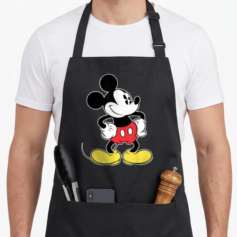 Funny crazy mouse man apron - Cartoon character standing with hands on hips in red shorts and yellow shoes — shown on a black cotton canvas apron against a white background