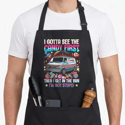 Stupid candy aprons - Retro van with rainbow and scattered lollipops. Text reads I Gotta See The Candy First Then I Get — shown on a black cotton canvas apron against a white background