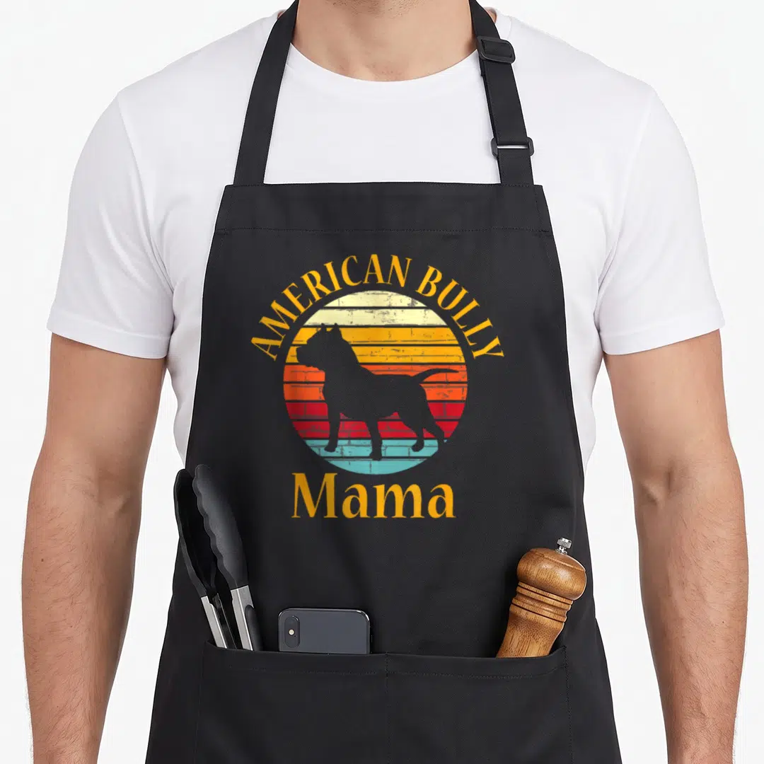 Bully dog apron - Grey American Bully silhouette inside a striped yellow orange red blue sunset circle with Mama text — shown on a black cotton canvas apron against a white background
