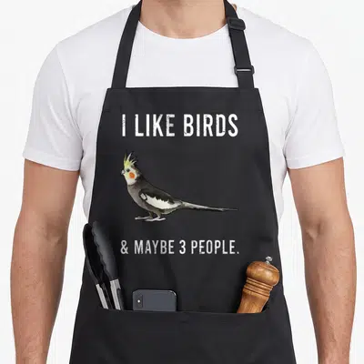Maybe bird apron - Cockatiel illustration flanked by white text reading I LIKE BIRDS & MAYBE 3 PEOPLE — shown on a black cotton canvas apron against a white background
