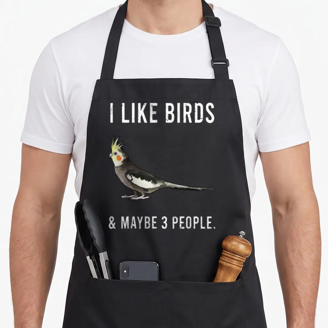 Maybe bird apron - Cockatiel illustration flanked by white text reading I LIKE BIRDS & MAYBE 3 PEOPLE — shown on a black cotton canvas apron against a white background