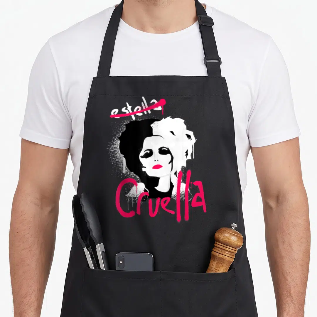 Cruella punk rock apron - Woman with split black and white hair, pink spray paint text estella and Cruella — shown on a black cotton canvas apron against a white background