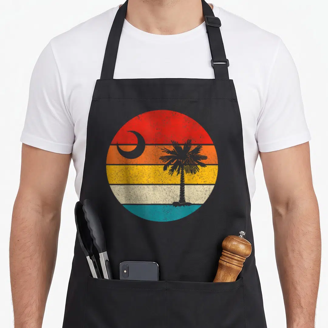 State flag pride apron - Retro circular graphic with grey palm tree and crescent moon on red orange yellow beige — shown on a black cotton canvas apron against a white background